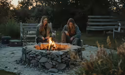 two women sitting around a fire pit, having a conversation
