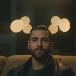 man with black shirt and leather jacket looking at camera