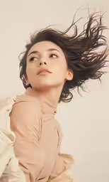 a woman in an off - white dress with long dark hair, looking upwards