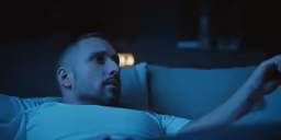 a young man laying in bed with a remote