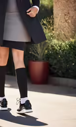 a person standing on a sidewalk wearing black and white socks and a black jacket and skirt