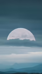 a large full moon shining through clouds over some mountains