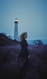 a young woman poses near a lighthouse at night