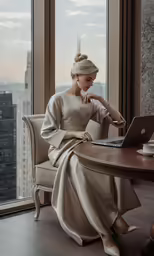a woman in a tan dress sitting at a table in front of a window