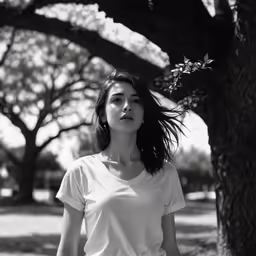 a girl standing outside by some trees looking into the camera
