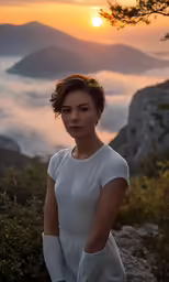 a woman stands on a cliff looking at the camera and in the foreground a sea of clouds, mountains, and sun rise