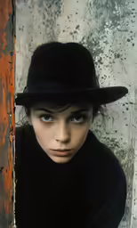 a young person wearing a hat standing in front of a dirty wall