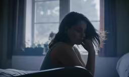 a woman sitting in front of a window and looking down