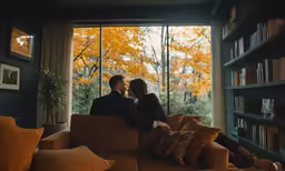 two people sit on the couch facing a large window