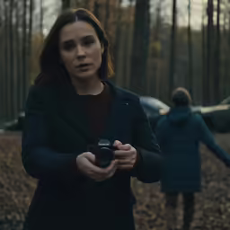 woman standing in woods with camera in front of her