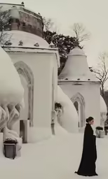 a woman in a black long dress walking through the snow