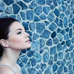 a woman stands near a stone wall as she looks away from the camera
