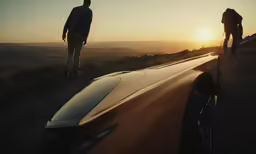 two men walking up a road near a car and sunset