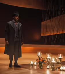a man in a black hat and coat near several candles