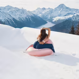 a woman sitting on a small air mattress on the snow covered mountain side