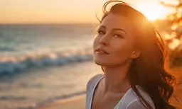 a woman standing on top of a beach with the sun setting