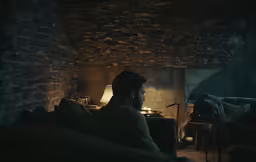 a woman sitting in a dimly lit room with a fireplace