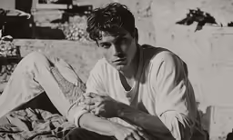 black and white photograph of young man sitting on floor with legs crossed