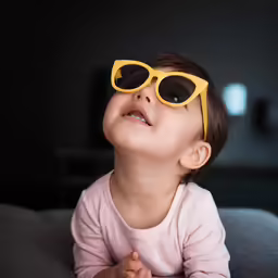 young baby wearing yellow sunglasses laying on a bed