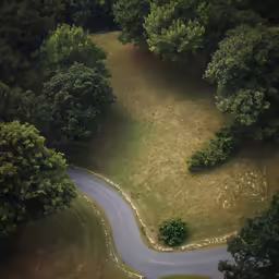 an aerial view of a curved country road with a forest area behind it