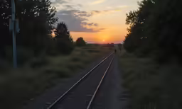 a sunset over a train track in a rural area