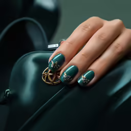 female hand with blue and gold manicures on their nails with green bag