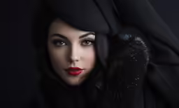 a woman in a fur trimmed scarf with her head covered by a black hood and dark eyes