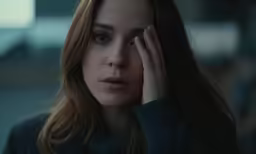 a woman with brown hair holds her face in front of the camera