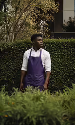 a man in a purple apron stands near a hedge
