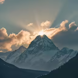 sun peeking through the clouds above a mountain