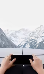 two hands hold up a smart phone above snowy mountains