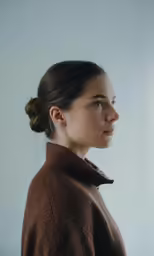 a woman with a brown sweater stares ahead