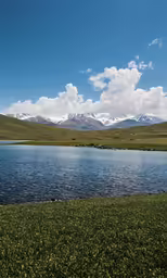 a clear blue body of water with snow capped mountains in the distance