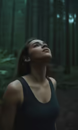 a woman stands in the woods looking up at something