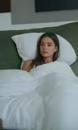 a woman sitting under an unmade bed