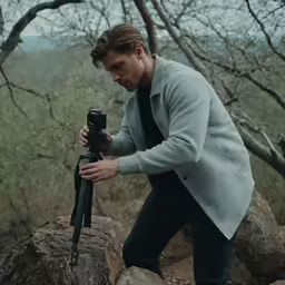 a man holding a camera on top of a rocky hillside