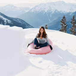 a young woman sitting on a pink snow tube in the middle of mountains
