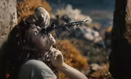 woman with her face covered by a gun as another looks at the ground