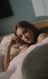 woman laying in bed holding pillow looking at camera