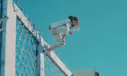 a girl climbs on the side of a metal fence