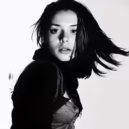 the young woman is posing with her hair blowing in the wind,a black and white photo of a woman