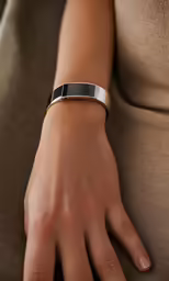 a woman is wearing a gold bracelet with black enamel