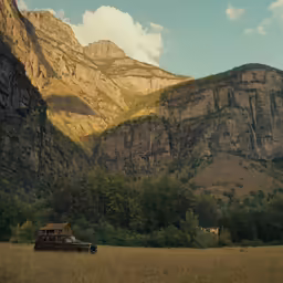 the mountains rise above a grassy field as an old truck travels by
