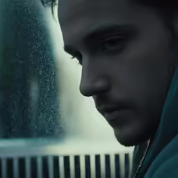 man looking through window with rain falling on him