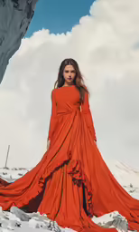 a woman posing in an orange gown, with a large rock face behind her