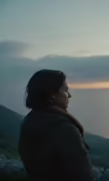 a woman looking out at the water on a cloudy day