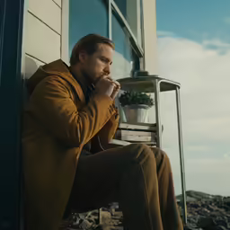 a man sits on steps outside of a window with his chin folded