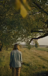 the woman is walking on the path under the tree