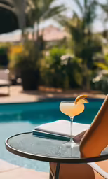 a glass of alcoholic drink and the back of a pool are shown