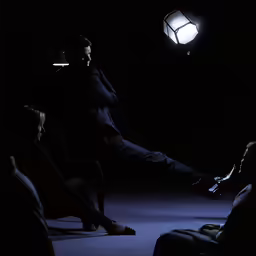 a man sits in the spotlight as he holds a cigarette